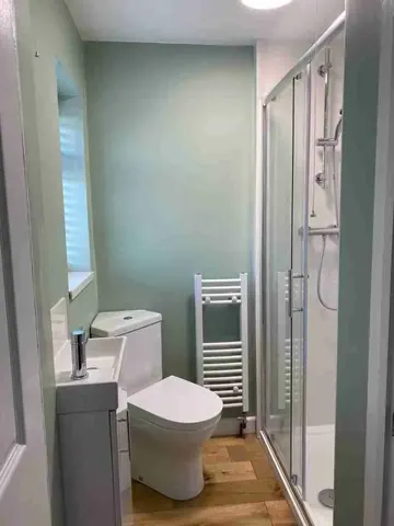 A small shower room with a sliding glass shower door, white toilet and basin, towel radiator and wood-effect floor